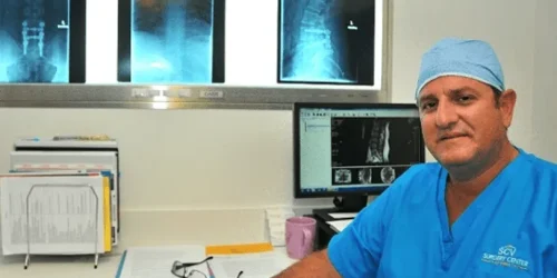 Doctor in blue scrubs reviewing X-rays in an office with a computer and files.