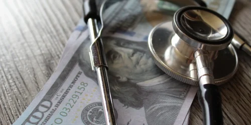 Hundred dollar bills and stethoscope depicting the high cost of spinal fusion surgery
