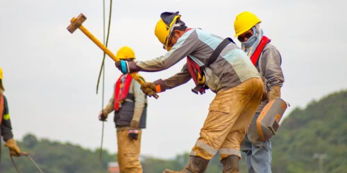 Construction workers in safety gear handling tools on a high steel beam.