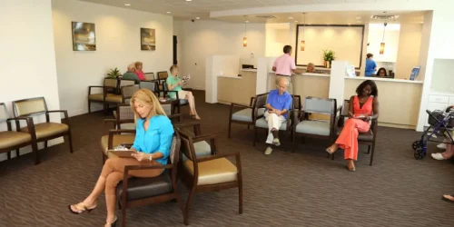People sitting in a spacious, well-lit waiting room with a reception desk.