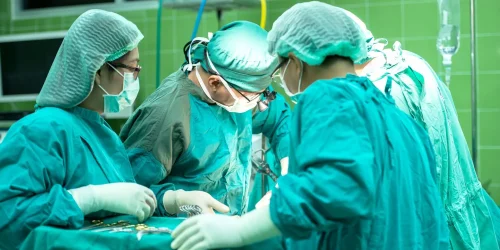 Four surgeons in scrubs operating in a green-tiled surgery room.