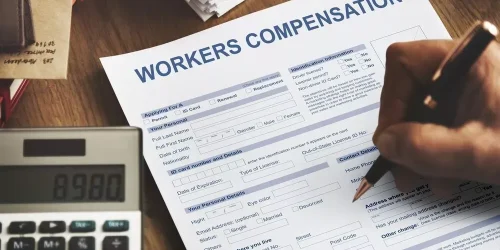 Person filling out a Workers' Compensation form with a calculator nearby.