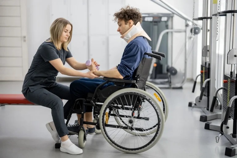 Therapist assists wheelchair user with arm exercises in a gym setting.
