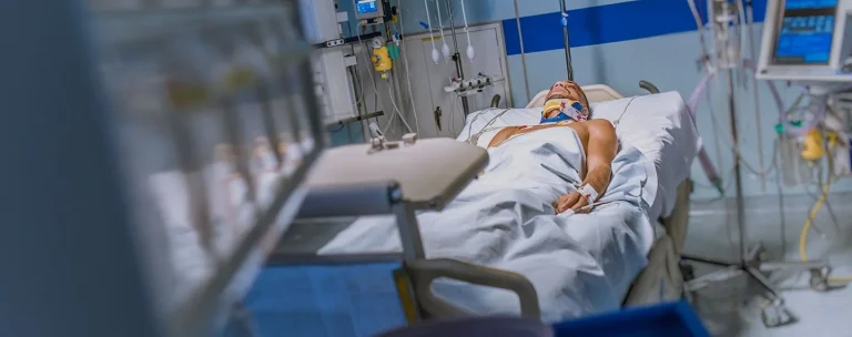 A patient with medical equipment lies in a hospital bed, surrounded by monitors.