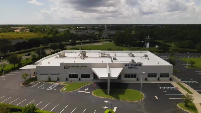 Aerial view of a modern surgery center with an adjacent parking lot and surrounding green landscape.