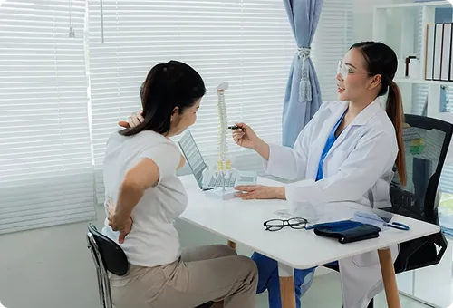 Doctor consults patient with back pain, showing spine model.