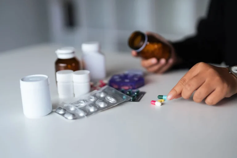 Person selecting pills from a variety of medicine bottles on a table.