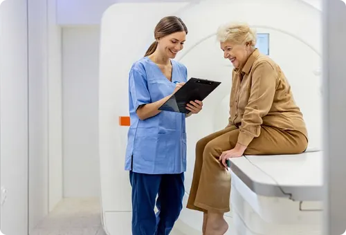 A healthcare worker talks with a patient seated on an MRI machine.