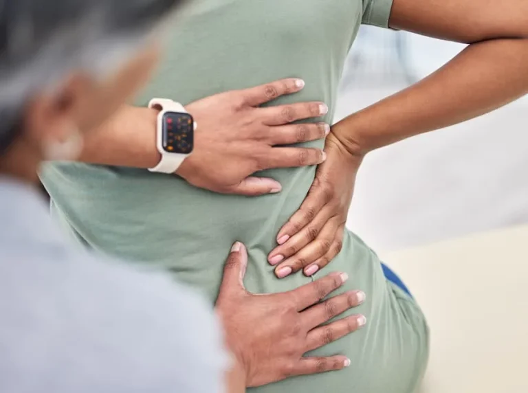 Person with back pain receiving a massage, showing hands on lower back.