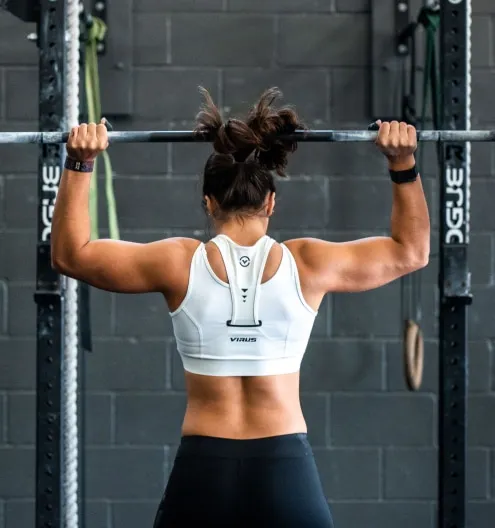 A woman in athletic wear performs a pull-up in a gym.