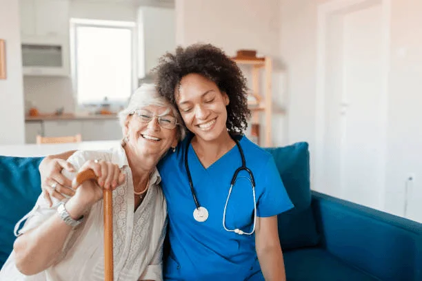 Patient Experience Nurse and elderly woman sitting on a couch, smiling together.