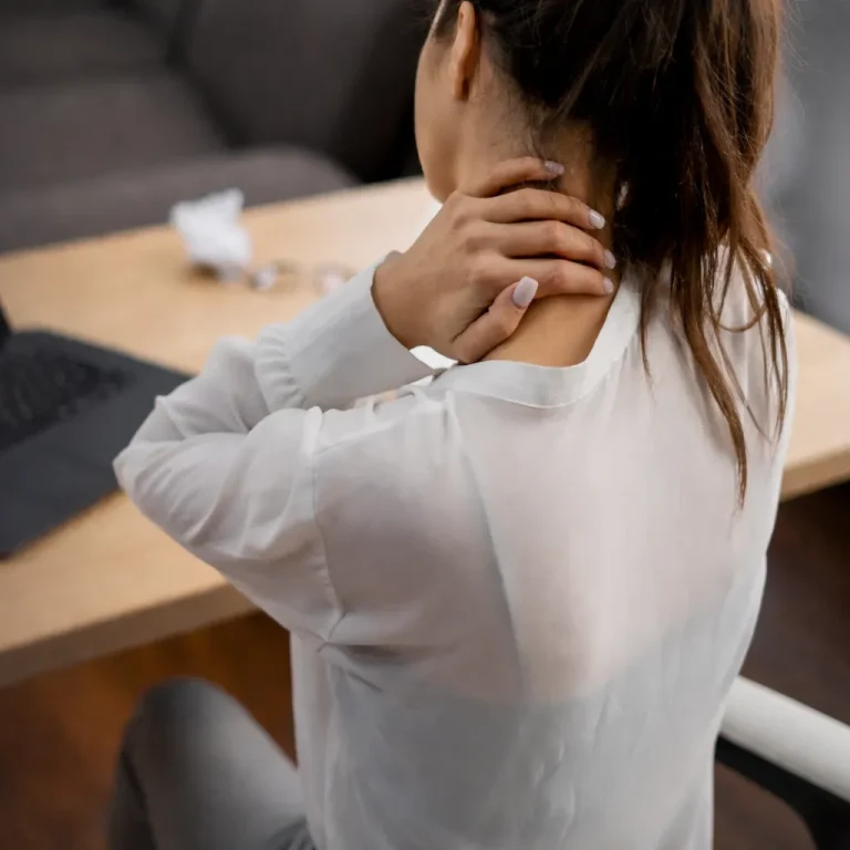Person sitting at a desk massaging their neck near a laptop.