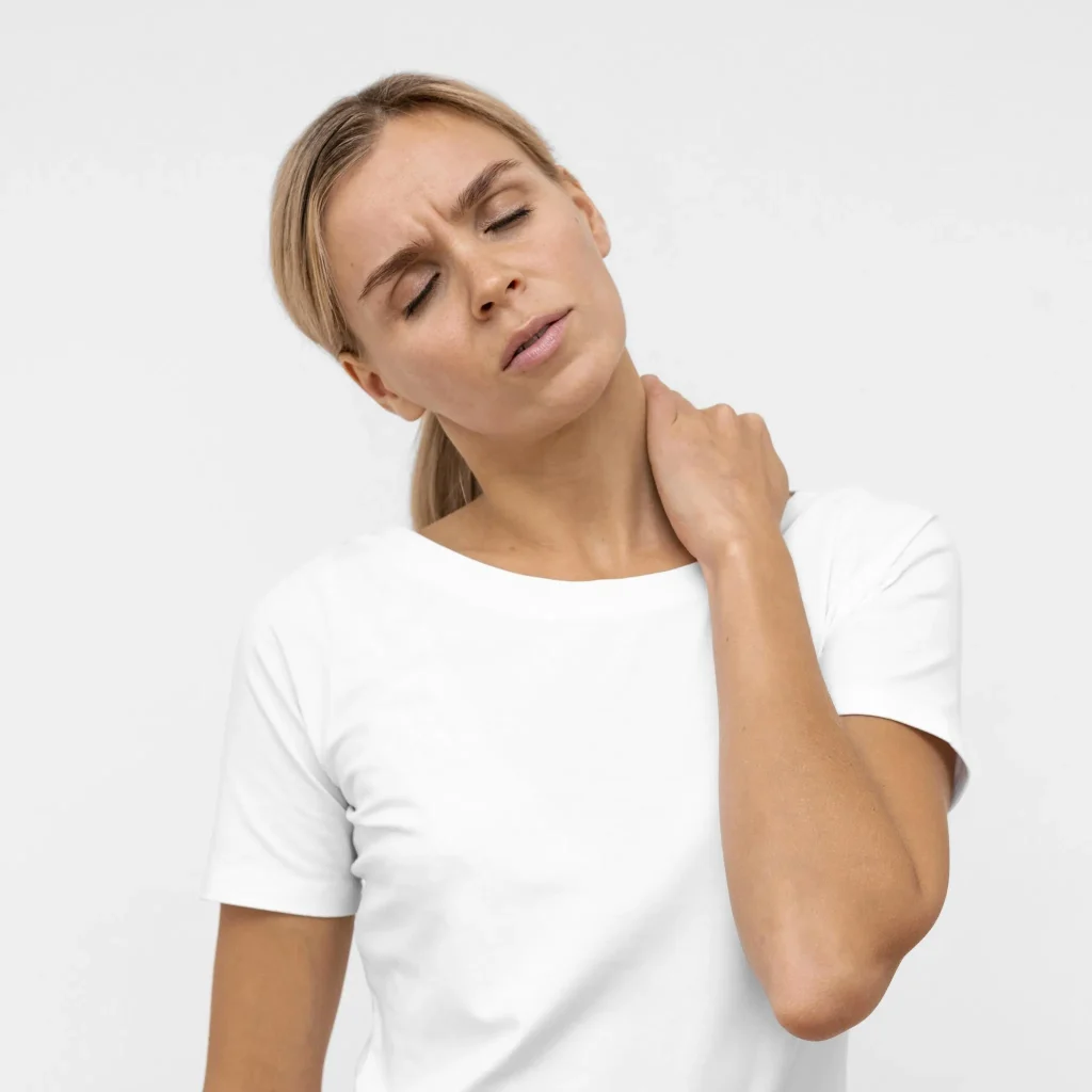 Woman in a white shirt holding her neck, looking in discomfort.
