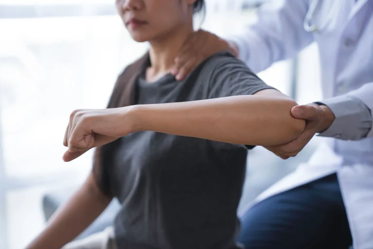 A doctor examines a patient's extended arm and shoulder.