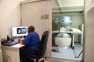 Man at desk reading imaging results, imaging machine in background.