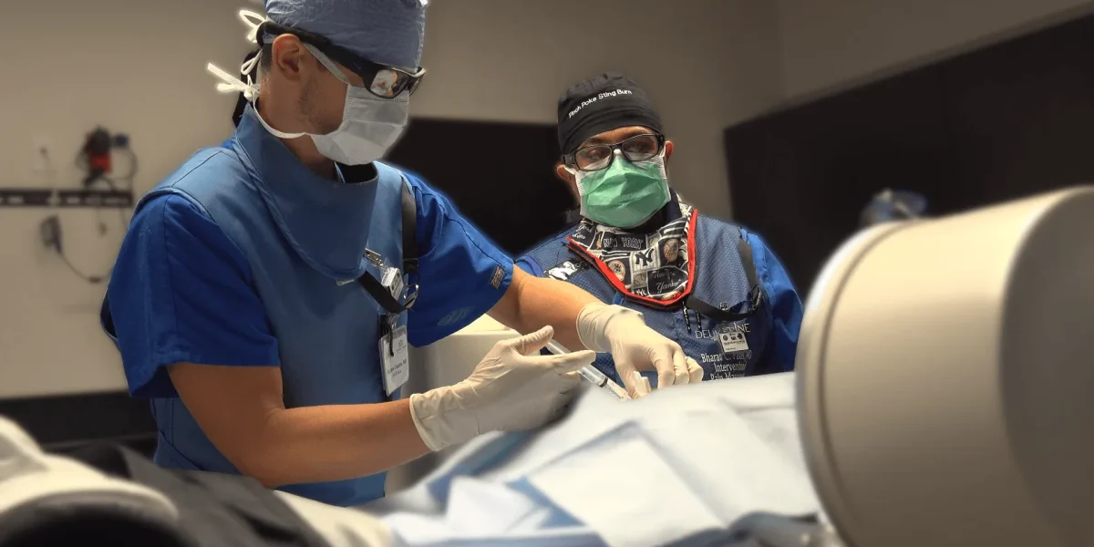 Two surgeons in blue scrubs perform a procedure, representing top spine surgeons at work.
