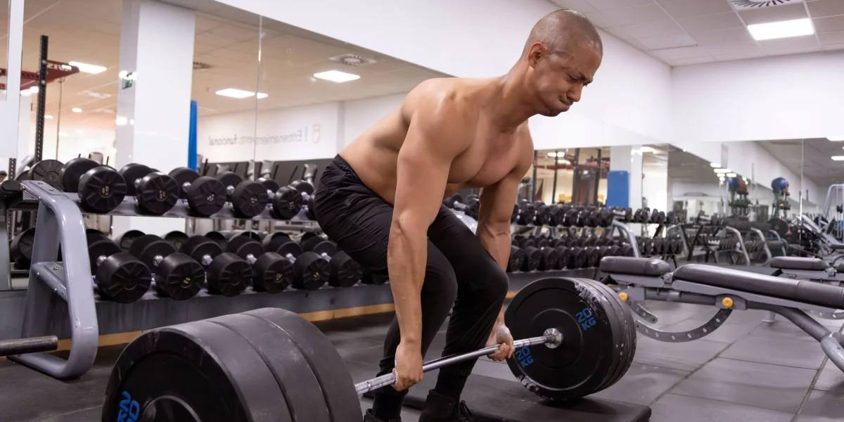 A man improperly lifting a heavy barbell in a gym, risking a herniated disc.